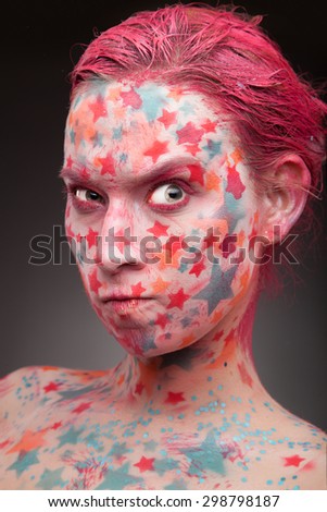 Emotional portrait of a young angry woman with stars on the face and painted hair in pink