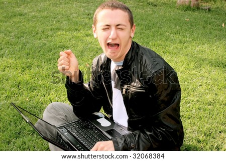 Crying boy with laptop on the grass.