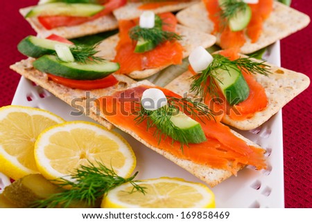 Salmon sandwiches with lettuce,  fresh and pickled cucumber, onion, lemon on plate.