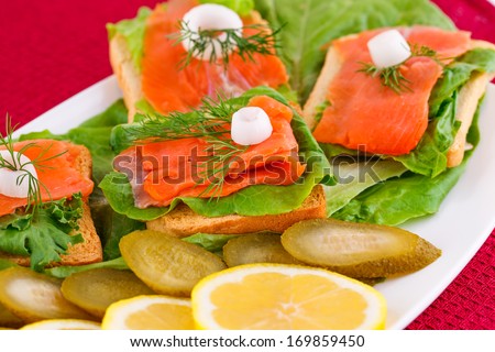 Salmon sandwiches with lettuce,  fresh and pickled cucumber, onion, lemon on plate.