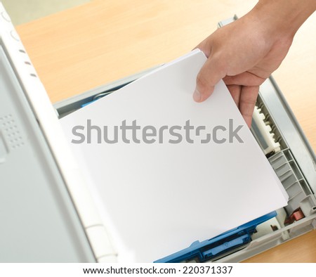 Male hand holding paper sheets into printer tray in office.