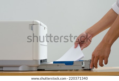 Male hand holding paper sheets into printer tray in office.