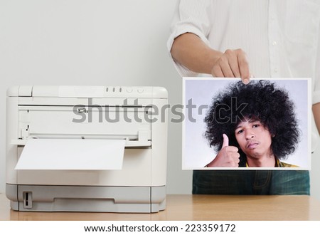 Businessman showing printed paper near color printer on table in office