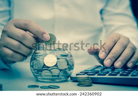 Vintage,businessman putting money coins into glass jar bank for saving and insurance concept
