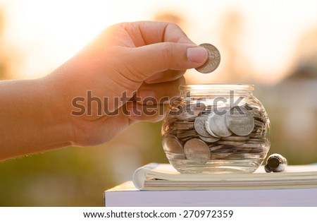 Male hand putting money coins on book with sunlight, Saving for education fund concept