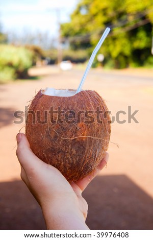 A girl holds out her hand with a coconut and a straw representing a nice cold tropical drink on the north shore of oahu hawaii.