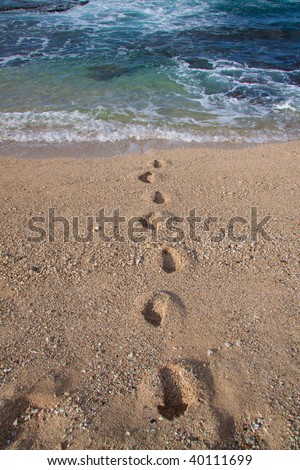 Foot prints are coming out of the water of a tropical beach in oahu hawaii.