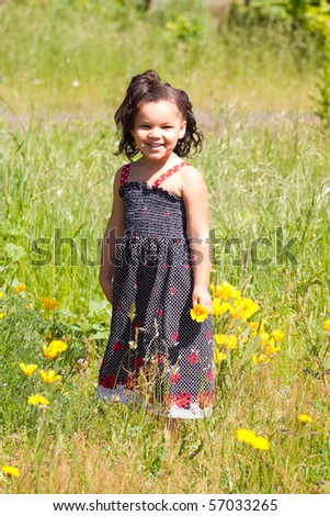 A young african american (black) girl stands in a field with a flower of yellow and white while wearing a black and red dress.