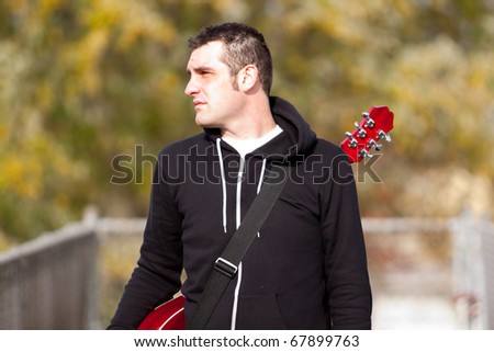 A guitar player stands outside while modeling himself and his guitar for a music promo photo shoot.