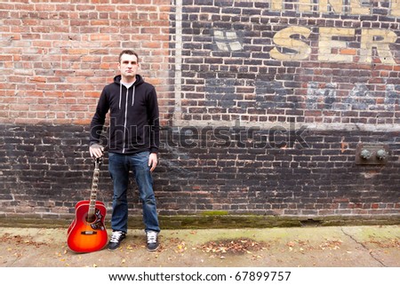 A guitar player stands outside while modeling himself and his guitar for a music promo photo shoot.