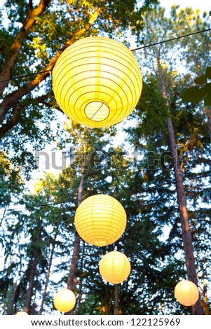 Yellow wedding decorations hang from the trees at a wedding ceremony and reception outdoors in Oregon. These yellow chinese lanterns or japanese lantersn are well lit.