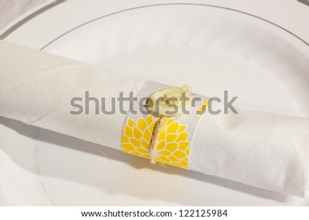 Silverware is wrapped up in a napkin for a wedding dinner reception in an old barn. The wedding decor includes a japanese or chinese influence with colors of white, grey (or gray) and yellow.