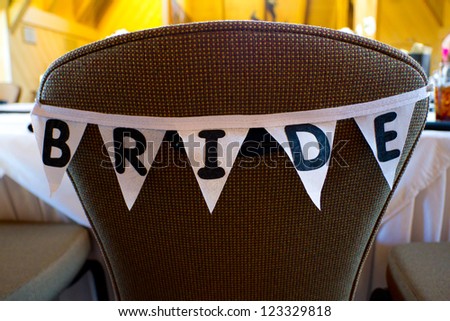 This chair at a wedding has a banner of flags that spell out the word bride to reserve her dinner seat.