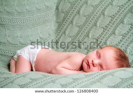 A newborn baby boy sleeps on a blanket over the couch while wearing nothing but a diaper.