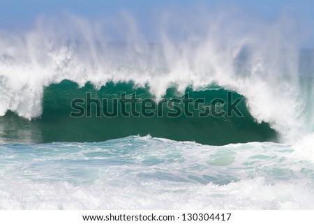 Large waves break off the north shore of oahu hawaii during a great time for surfers surfing. These waves have hollow barrells and are located at pipeline by sunset beach.