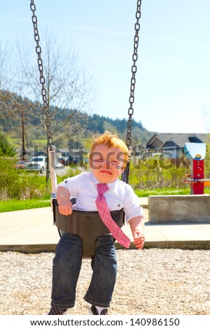 A baby boy sits on a swing set while upset and crying wearing nice clothes.