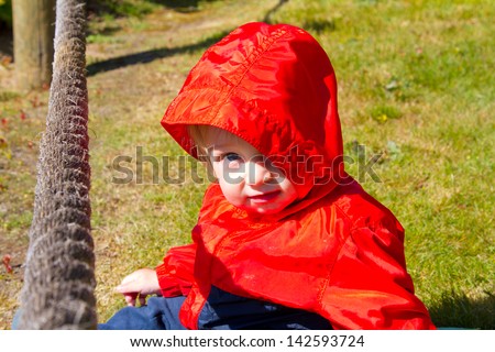 A kid in a red jacket hangs out at the beach while playing near some old weathered ropes along the coastline in this simple potrait.