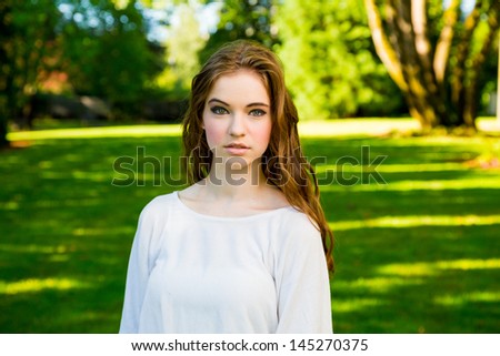 A beautiful young girl poses for a fashion style portrait outdoors at a park with natural lighting.