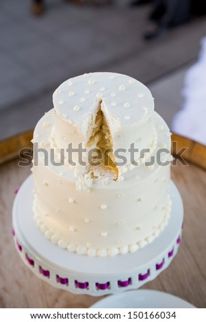 A white wedding cake is cut after the bride and groom cut the cake at their wedding reception.