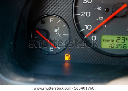 A gas guage in a car reads empty and shows the warning light to let the driver know they are out of gas and need to refuel.