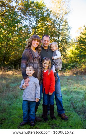 Nuclear family of five people including a mother father and three children stand together outdoors for this family picture.