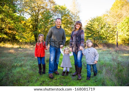 Nuclear family of five people including a mother father and three children stand together outdoors for this family picture.