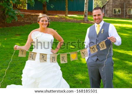 A bride and groom hold a banner of burlap that reads thank you so they can use it later for their thank you cards.