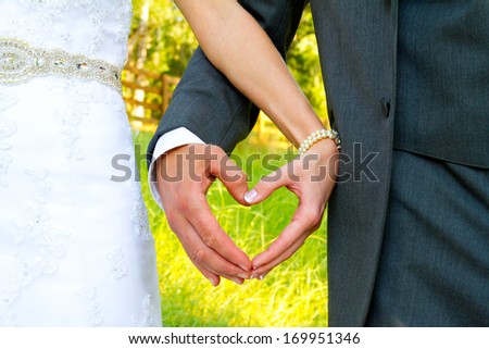 Heart shape is formed by the bride and groom putting their hands together while standing outside in a country field on their wedding day.