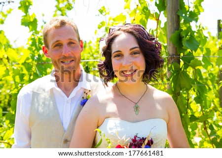 Bride and groom sharing a moment and posing for the camera in this portrait of the two people in a vineyard at a winery on their wedding day.