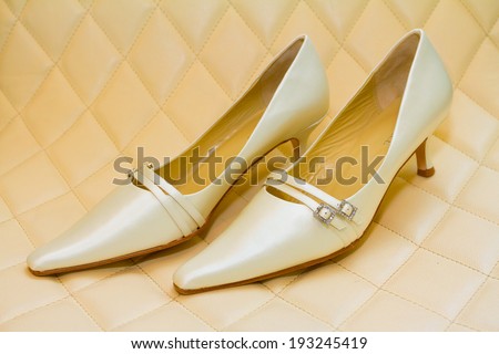 White wedding shoes to be worn by the bride on her ceremony day. This fashion image isolates the heels on their own on a leather couch.