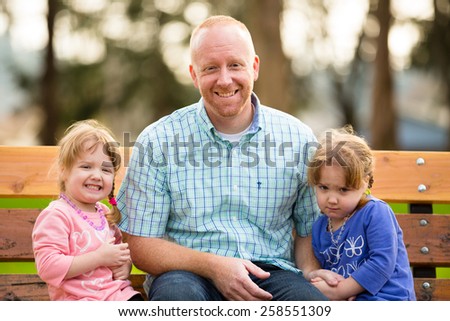 Dad with two daughters that are identical twins at a park in natural light.