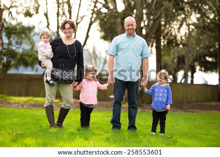 Lifestyle photo of a family of five including mother, father, and three daughters. Two daughters are identical twins.