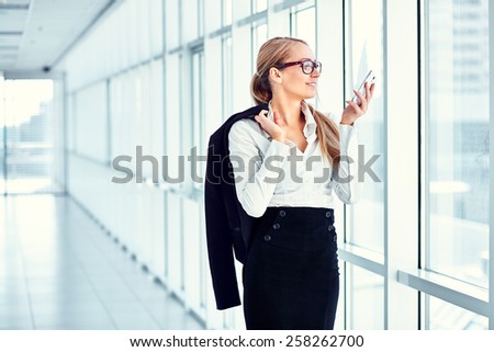 Beautiful business woman looking at mobile phone in the hallway