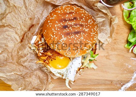 Top view of burger with egg, bacon, tomato ketchup on a wooden board