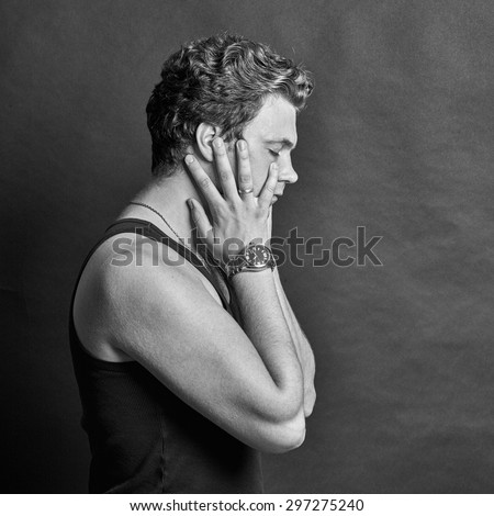 Black and white portrait of young man holding his head to calm a headache on a gray background