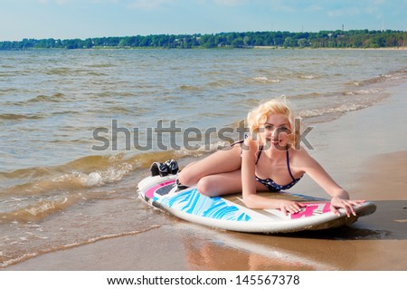 Pretty blond girl model like Marilyn Monroe with surfing board on a beach.