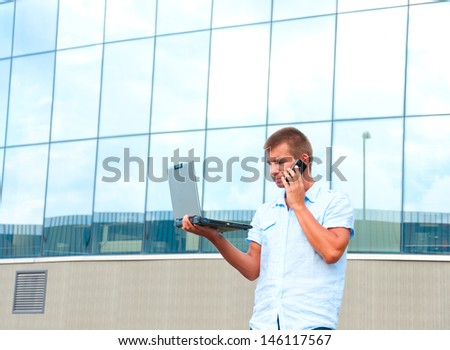Business man with laptop and mobile phone in front of modern business building.