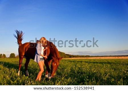 Young woman walking with a horse in the field.