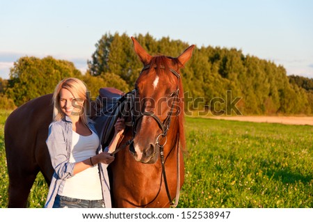 Young woman walking with a horse in the field.