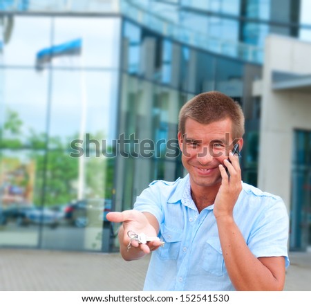 Business man speaking on phone and holding apartament key in front of modern business building.