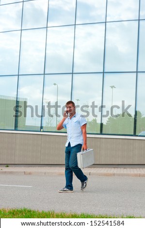 Business man with metal case and mobile phone in front of modern business building.