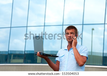 Business man with laptop and mobile phone in front of modern business building.