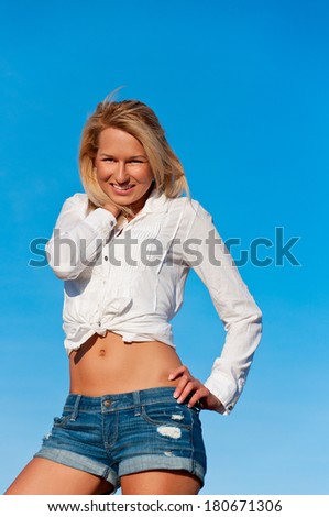 Beautiful woman in jeans short and white shirt posing on a wheat bale in a field