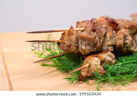 grill meat on a sticks with green on wooden plate.