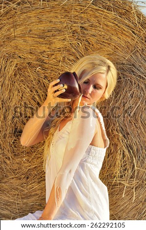 Happy woman drinking milk from cruse or crock and hay as background