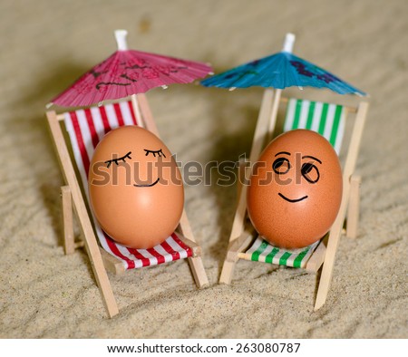 easter funny eggs sitting on a chair under umbrella on a sand. selective soft focus
