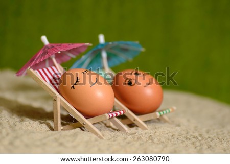 easter funny eggs sitting on a chair under umbrella on a sand. selective soft focus