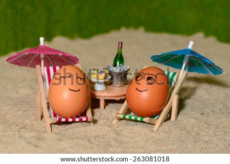 easter funny eggs sitting on a chair under umbrella on a sand and bottle of champagne in a  bucket. selective soft focus
