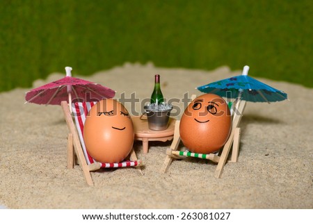 easter funny eggs sitting on a chair under umbrella on a sand and bottle of champagne in a  bucket. selective soft focus