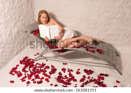 Woman in a salt room with red roses and petals reading a book